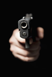 Eine Hand hält eine Pistole und richtet sie auf die Kamera, schwarzer Hintergrund - FSIF00661