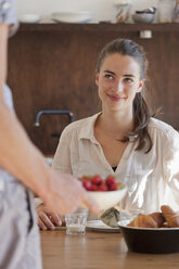 Junge Frau sitzt am Esstisch mit Frühstück, lächelnd - FSIF00712
