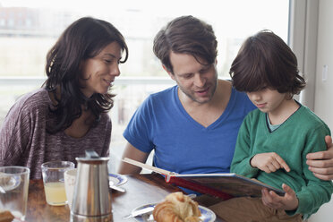 Familie am Esstisch beim Lesen eines Buches - FSIF00797
