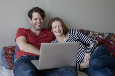 Couple using laptop while lying on sofa - FSIF00801