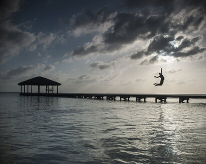 Silhouette person jumping into sea against cloudy sky at dusk - FSIF00826
