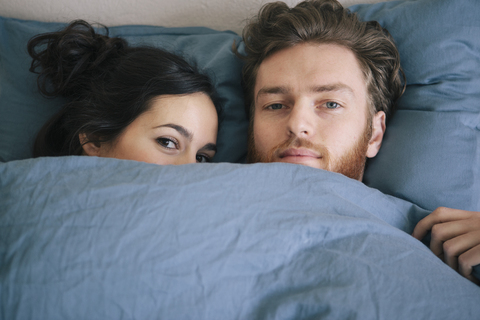 Porträt eines jungen Liebespaares unter der Bettdecke im Bett, lizenzfreies Stockfoto