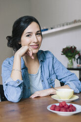 Porträt einer glücklichen jungen Frau, die am Tisch in der Küche sitzt - FSIF00855