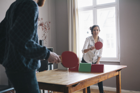 Junge Frau spielt Tischtennis mit Mann zu Hause, lizenzfreies Stockfoto