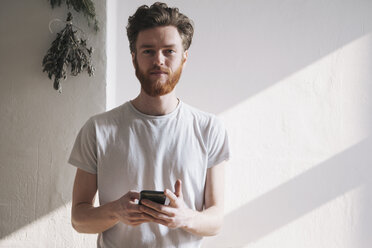 Portrait of confident young man holding mobile phone at home - FSIF00873