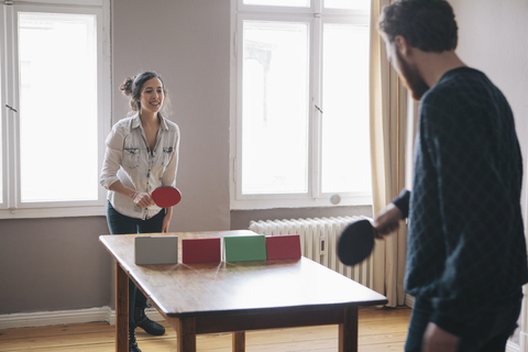 Junge Frau spielt Tischtennis mit Mann zu Hause, lizenzfreies Stockfoto