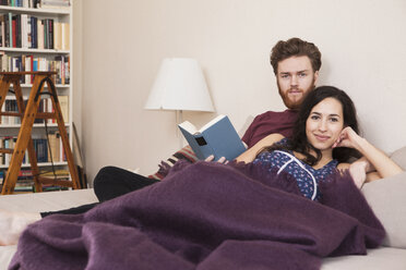 Porträt einer glücklichen jungen Frau mit einem Mann, der ein Buch im Bett hält - FSIF00876