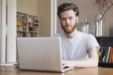 Porträt eines selbstbewussten jungen Mannes, der einen Laptop am Tisch benutzt - FSIF00881