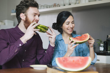 Glückliches junges Paar isst Wassermelone am Küchentisch - FSIF00886