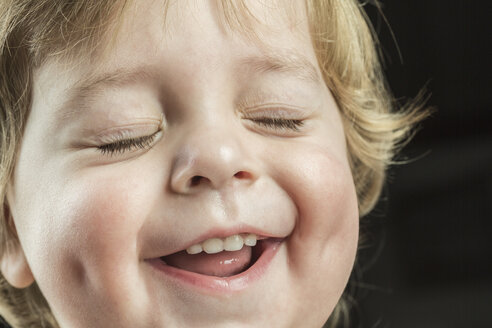 Close-up of cheerful boy with eyes closed over black background - FSIF00898