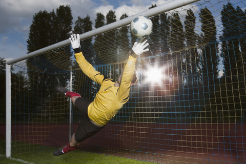 Full length of soccer goalkeeper diving to block ball stock photo