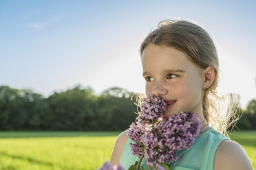 Glückliches Mädchen riecht an lila Blumen auf einem Feld - FSIF00935