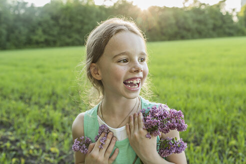 Fröhliches Mädchen hält lila Blumen auf einem Feld - FSIF00936