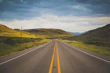 Road leading towards green mountains against cloudy sky - FSIF00972