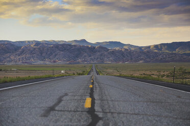 Road leading towards rocky mountains against cloudy sky - FSIF00975