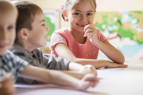 Porträt eines glücklichen kleinen Mädchens mit Freunden am Tisch im Klassenzimmer - FSIF00980