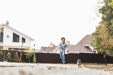 Boy running with dog on footpath against clear sky - FSIF00995