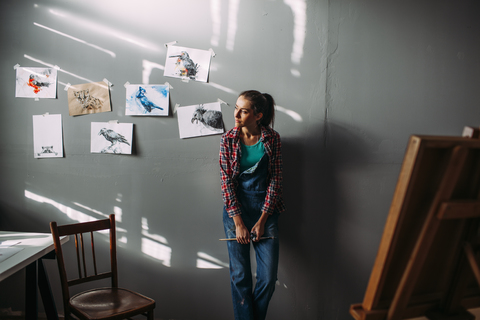 Thoughtful painter leaning on wall in art studio stock photo