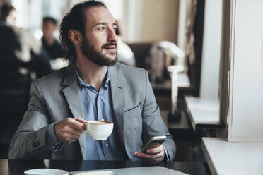 Mid adult businessman holding coffee cup and mobile phone in cafe - FSIF01019