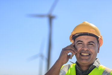 Porträt eines lächelnden Technikers mit Mobiltelefon in einem Windpark - ZEF14958