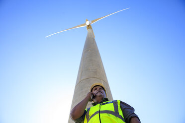 Low angle view of technician on cell phone in front of wind turbine - ZEF14963