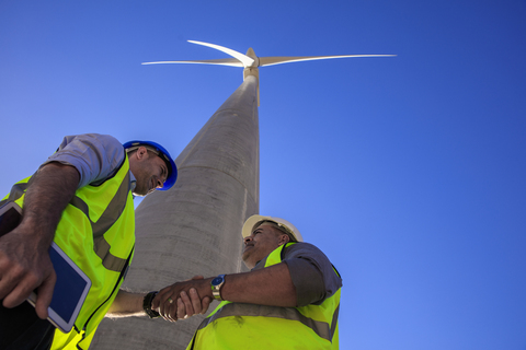Low angle view of technicians shaking hands in front of wind turbine stock photo