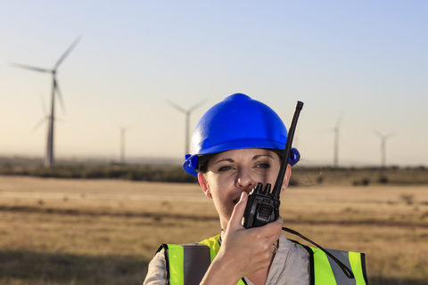 Technikerin mit Walkie-Talkie in einem Windpark, lizenzfreies Stockfoto