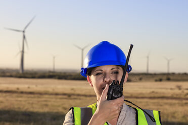 Female technician using walkie-talkie on a wind farm - ZEF14982