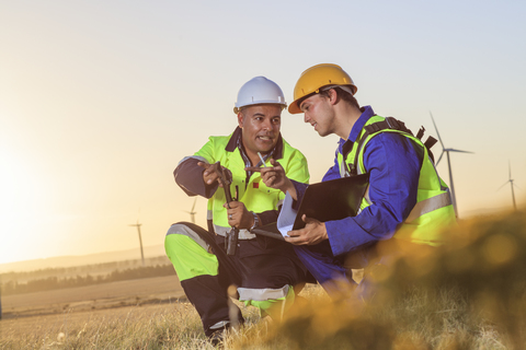 Zwei Techniker diskutieren bei Sonnenuntergang über einen Windpark, lizenzfreies Stockfoto