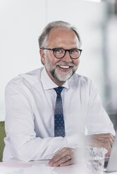 Portrait of happy mature businessman sitting at desk in office - UUF12724