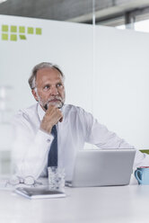 Mature businessman with laptop at desk in office thinking - UUF12725