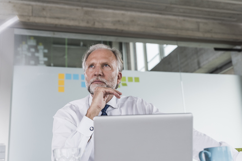 Mature businessman with laptop at desk in office thinking stock photo