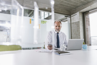 Älterer Geschäftsmann arbeitet am Schreibtisch im Büro - UUF12730