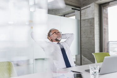 Smiling mature businessman at desk in office leaning back - UUF12734