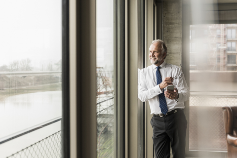 Smiling mature businessman standing at the window looking out stock photo