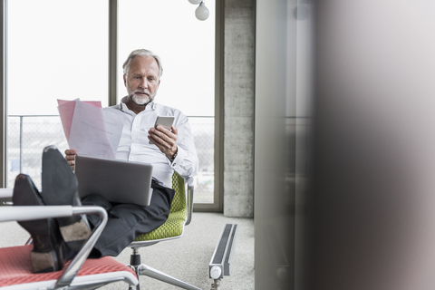 Mature businessman working on office chair with feet up stock photo