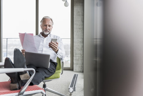 Älterer Geschäftsmann arbeitet auf einem Bürostuhl mit hochgelegten Füßen - UUF12748