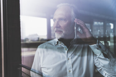 Portrait of mature businessman at the window talking on cell phone - UUF12750