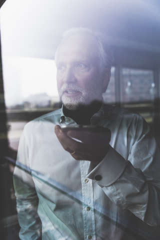 Portrait of mature businessman at the window using cell phone stock photo