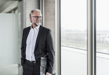 Lächelnder reifer Geschäftsmann, der am Fenster steht und hinausschaut - UUF12753