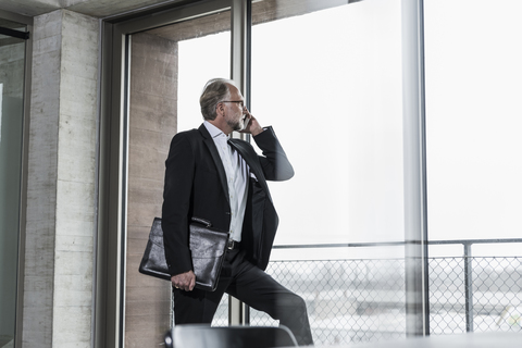 Älterer Geschäftsmann am Fenster, der mit einem Handy telefoniert, lizenzfreies Stockfoto