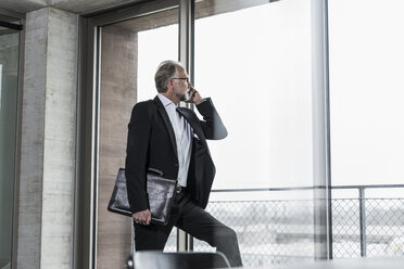 Mature businessman at the window talking on cell phone - UUF12754