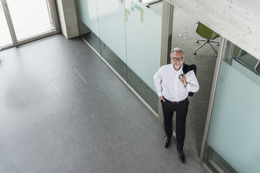 Elevated view of smiling mature businessman standing in office - UUF12761