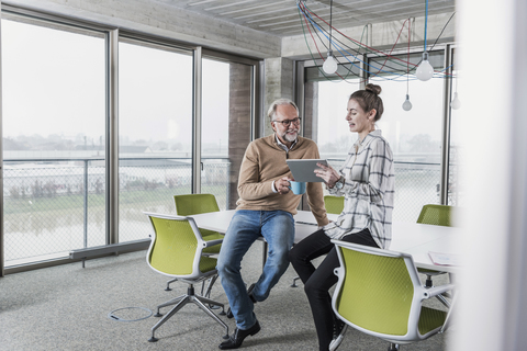 Lässiger reifer Geschäftsmann und junge Frau mit Tablet im Konferenzraum im Büro, lizenzfreies Stockfoto