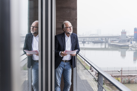 Mature businessman standing on balcony holding papers stock photo