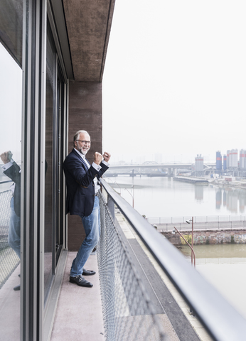 Happy mature businessman standing on balcony cheering stock photo