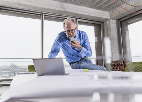 Älterer Geschäftsmann mit Laptop und Smartphone im Konferenzraum im Büro - UUF12799