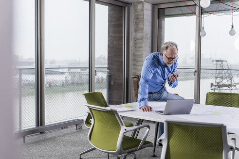 Älterer Geschäftsmann mit Laptop und Smartphone im Konferenzraum im Büro - UUF12800