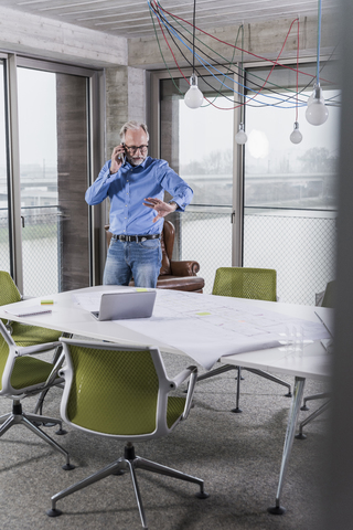 Älterer Geschäftsmann, der im Konferenzraum im Büro mit seinem Smartphone spricht, lizenzfreies Stockfoto