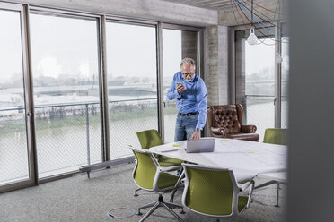 Mature businessman using laptop and smartphone in conference room in office - UUF12802